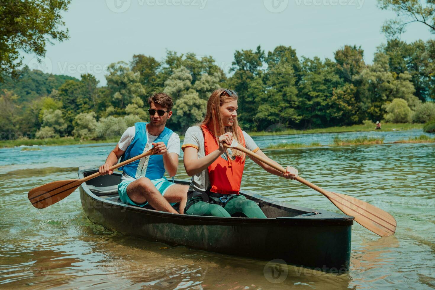 Couple adventurous explorer friends are canoeing in a wild river surrounded by the beautiful nature photo