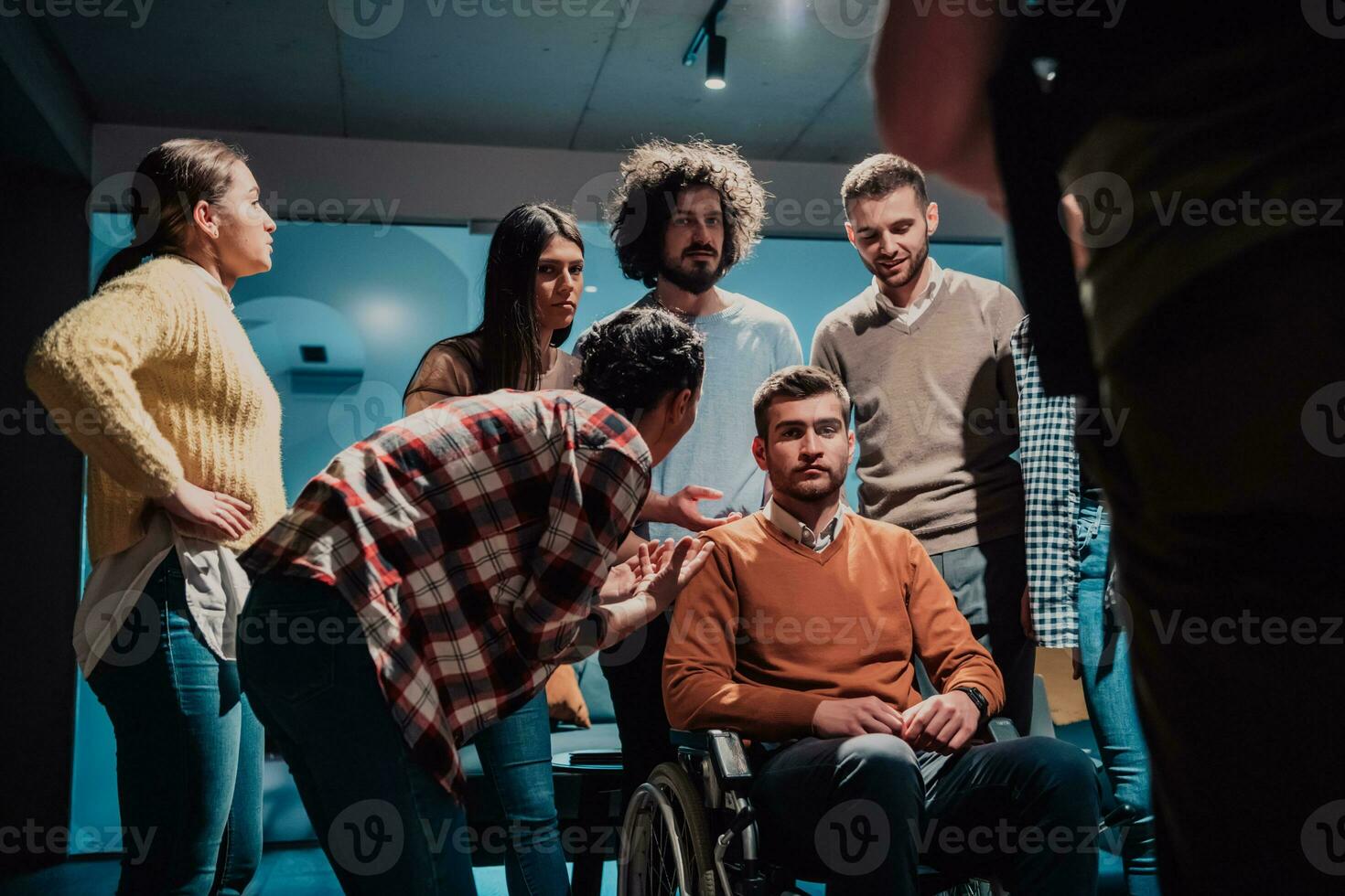 colegas ayuda su amigo en un silla de ruedas a tomar su primero pasos en un moderno oficina después un grave enfermedad foto