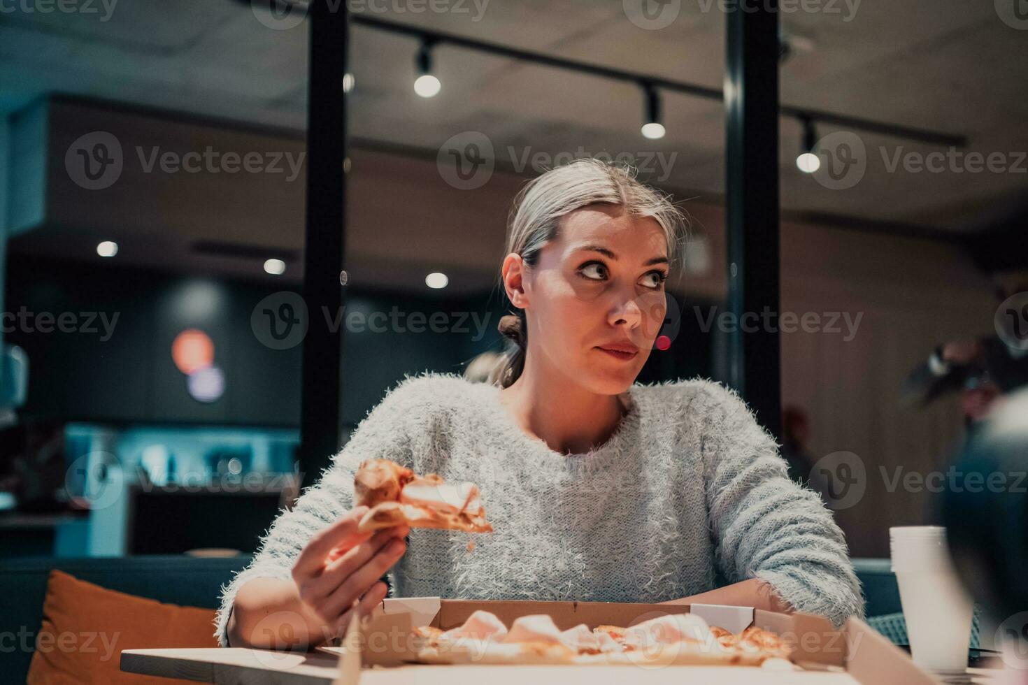 A modern blonde eating pizza in her office on a break from work photo