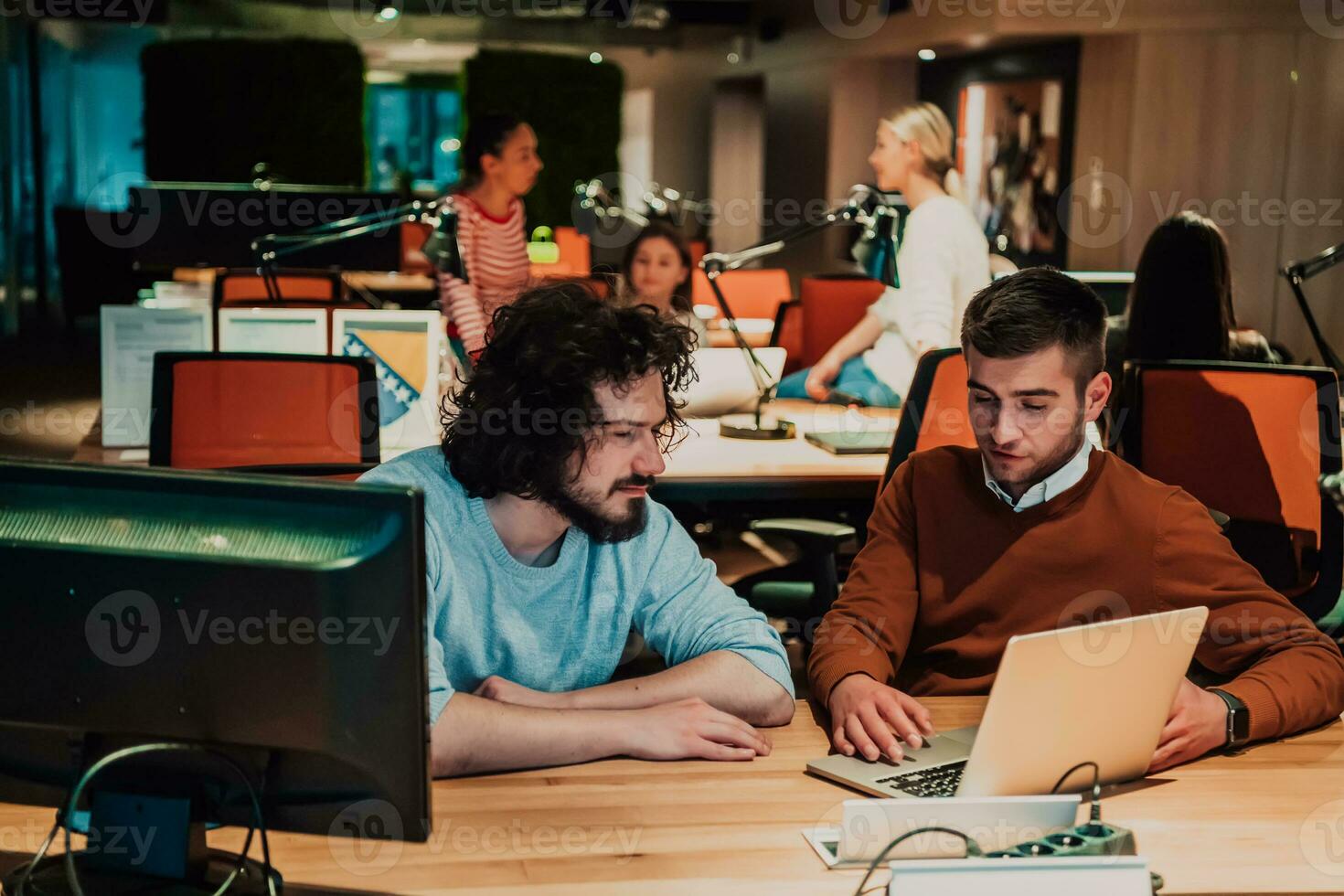Two business friends discuss a joint project while using a laptop in a fashionable office photo