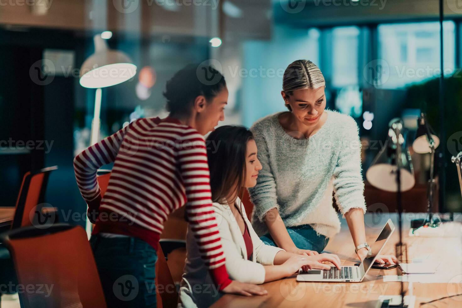 Tres joven mujer en un moderno oficina resolver un problema juntos mientras utilizando un ordenador portátil foto