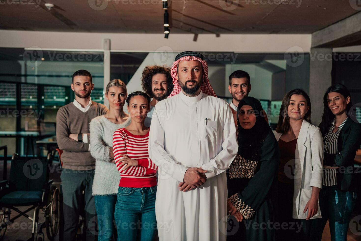 A diverse group of successful business people in a modern glass office stand together at the top with their Arab leader director photo
