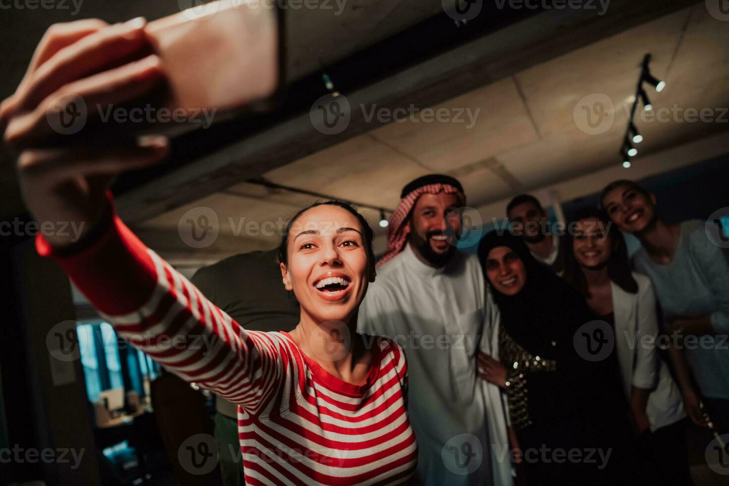 Diverse team of businessmen taking selfie photos on smartphone while in modern office
