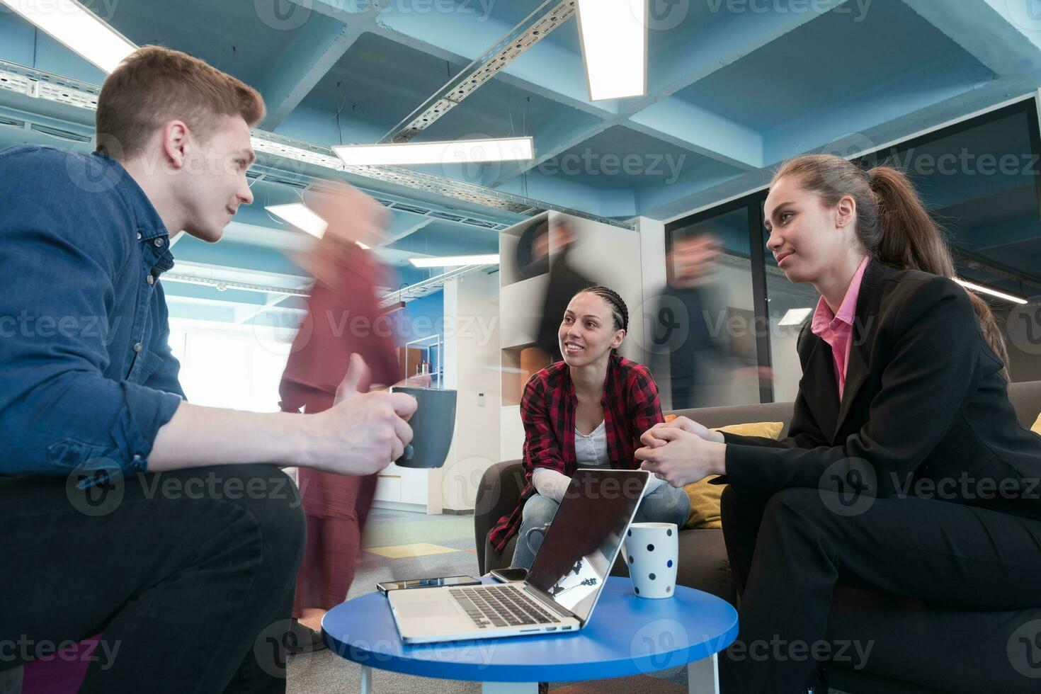 Multiethnic startup business team on meeting in a modern bright open space coworking office. Brainstorming, working on laptop. Group of coworkers walking around in motion blur. photo