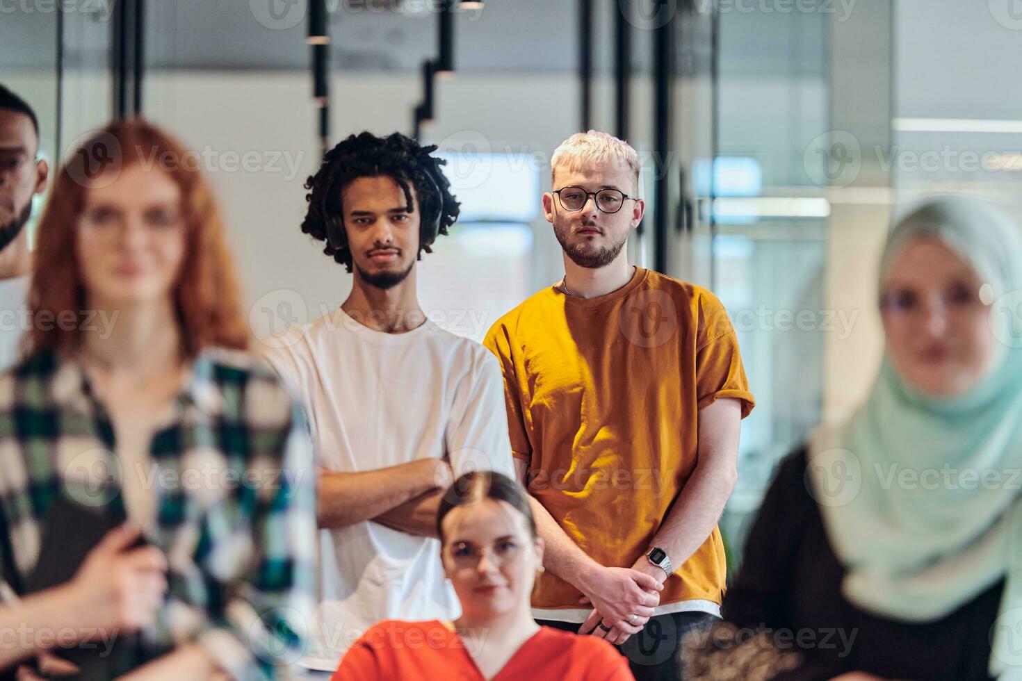 A diverse group of young business people congregates within a modern startup's glass-enclosed office, featuring inclusivity with a person in a wheelchair, an African American young man , and a hijab-clad woman, showcasing a dynamic blend of innovation and photo