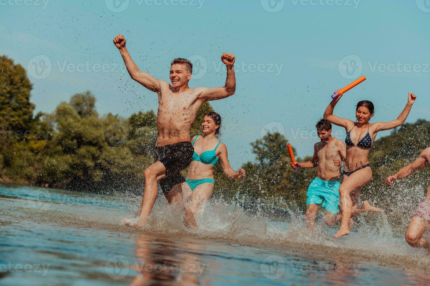 A group of diverse young people having fun together as they run along the river and play water games photo