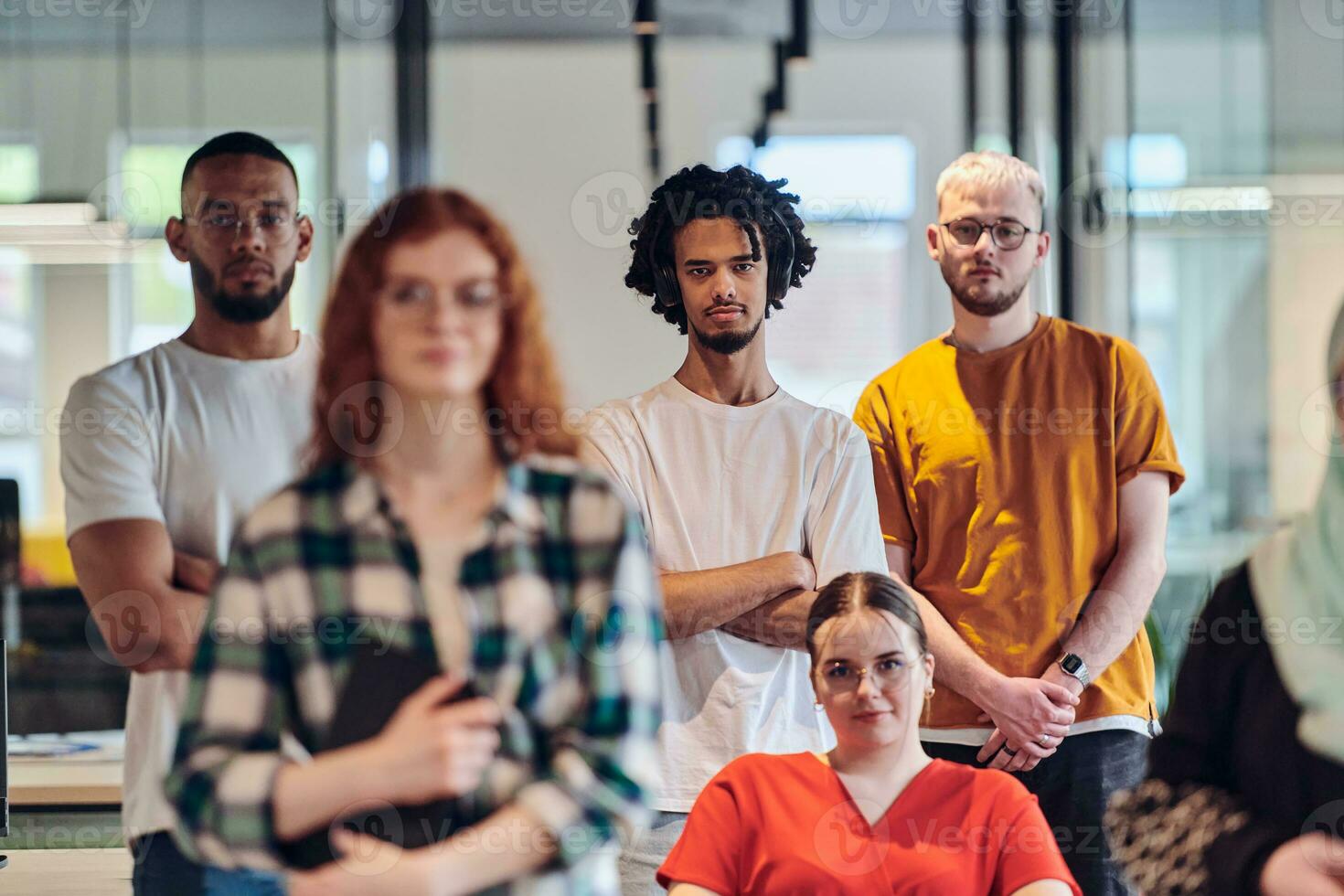 A diverse group of business people walking a corridor in the glass-enclosed office of a modern startup, including a person in a wheelchair and a woman wearing a hijab, showing a dynamic mix of innovation and unity. photo