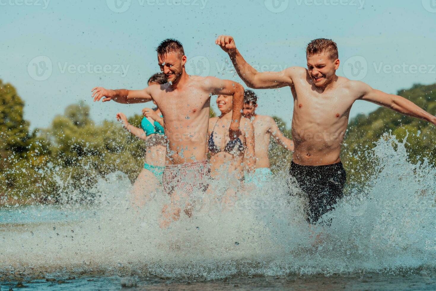 A group of diverse young people having fun together as they run along the river and play water games photo