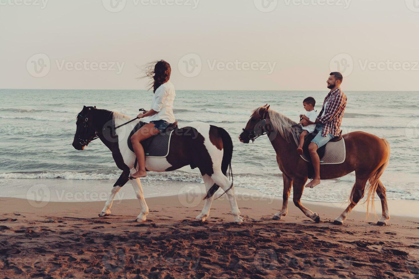 The family spends time with their children while riding horses together on a sandy beach. Selective focus photo