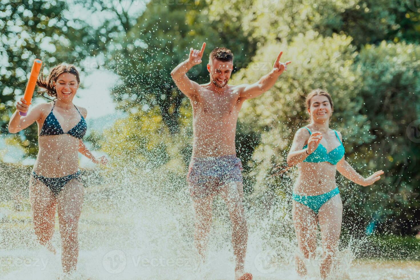 A group of diverse young people having fun together as they run along the river and play water games photo