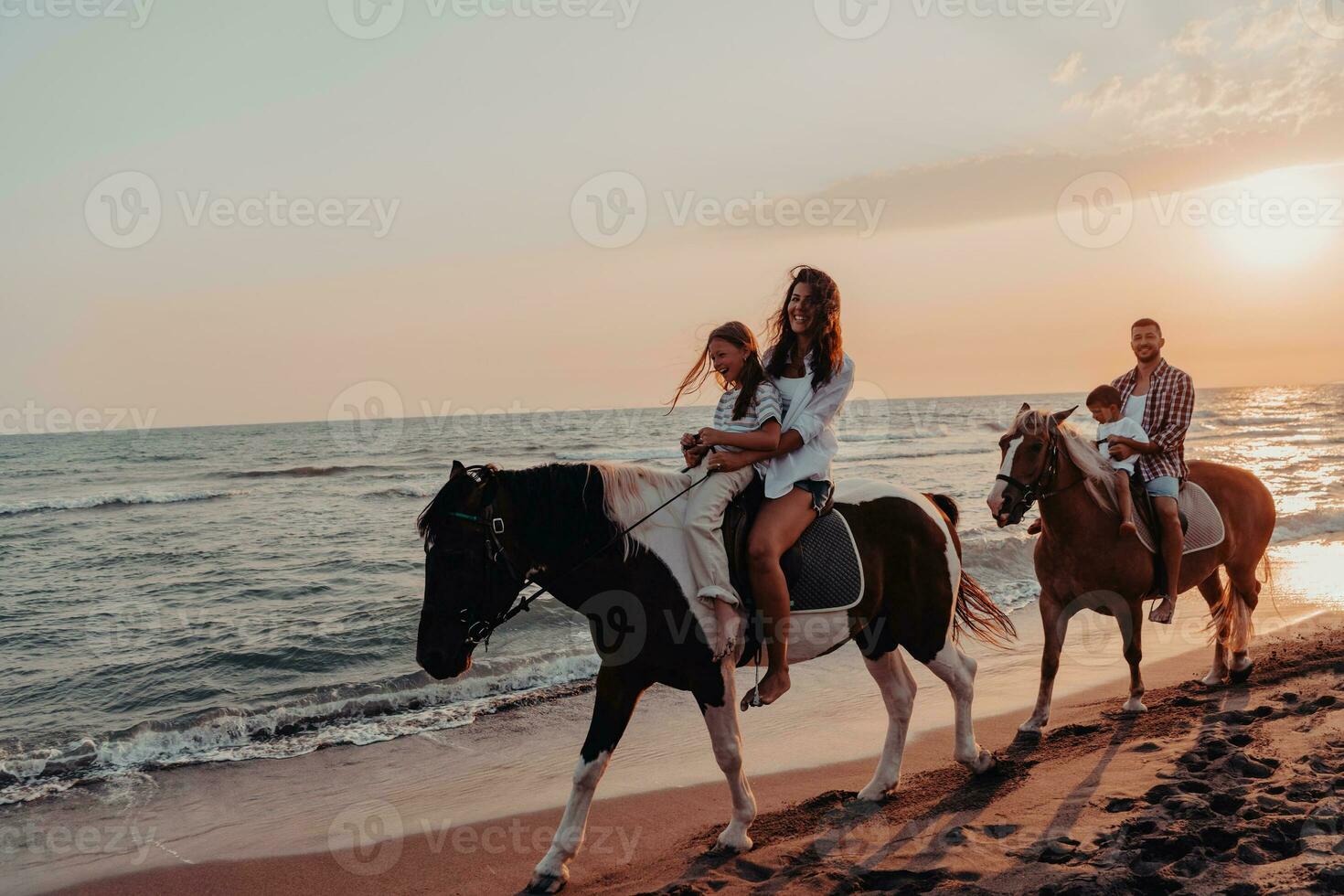 The family spends time with their children while riding horses together on a sandy beach. Selective focus photo