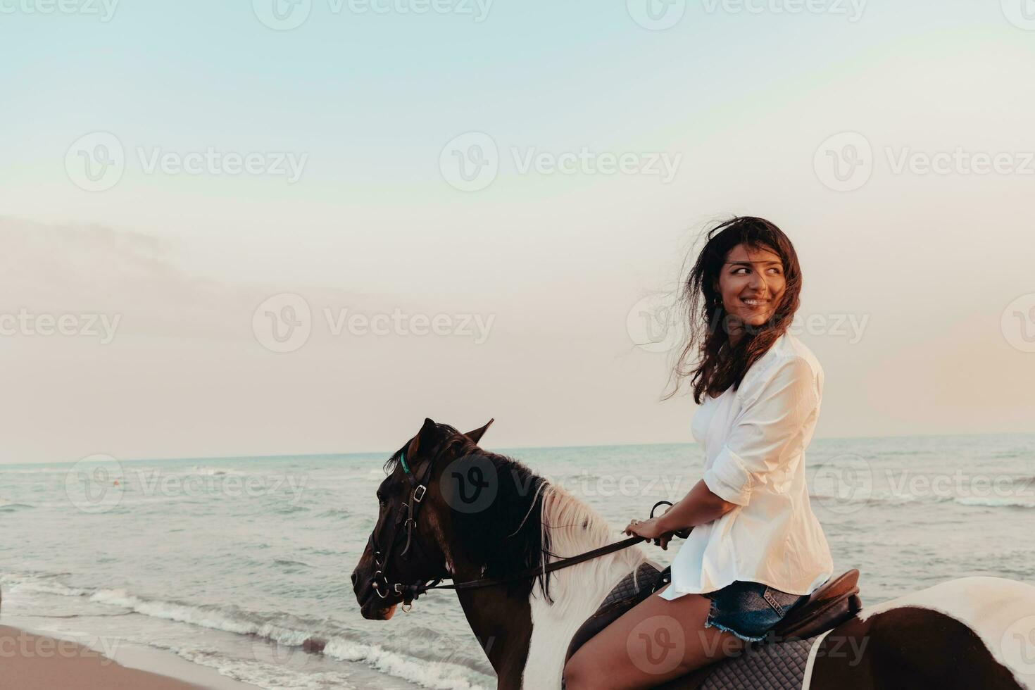 Woman in summer clothes enjoys riding a horse on a beautiful sandy beach at sunset. Selective focus photo