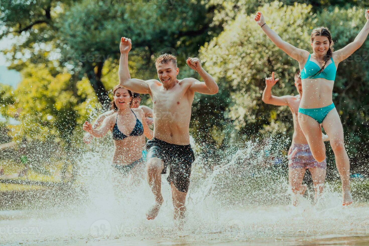 A group of diverse young people having fun together as they run along the river and play water games photo