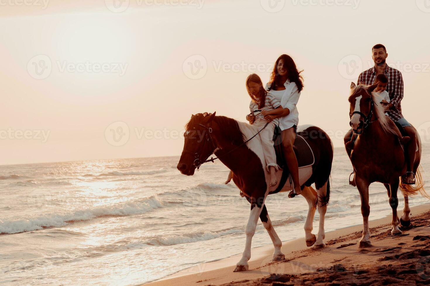 The family spends time with their children while riding horses together on a sandy beach. Selective focus photo