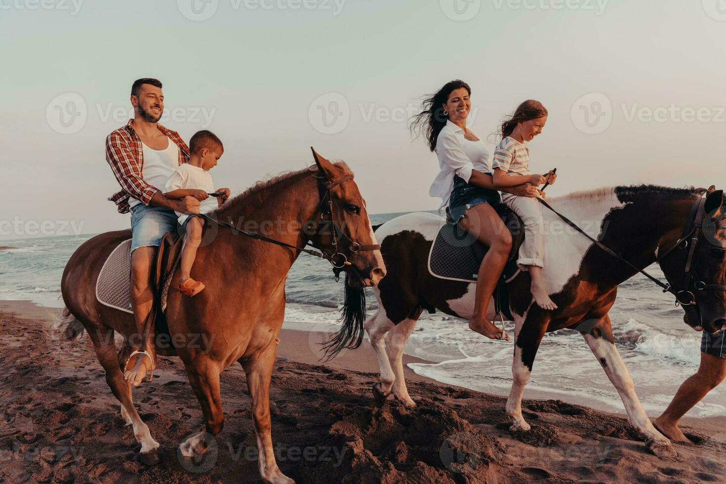 The family spends time with their children while riding horses together on a sandy beach. Selective focus photo