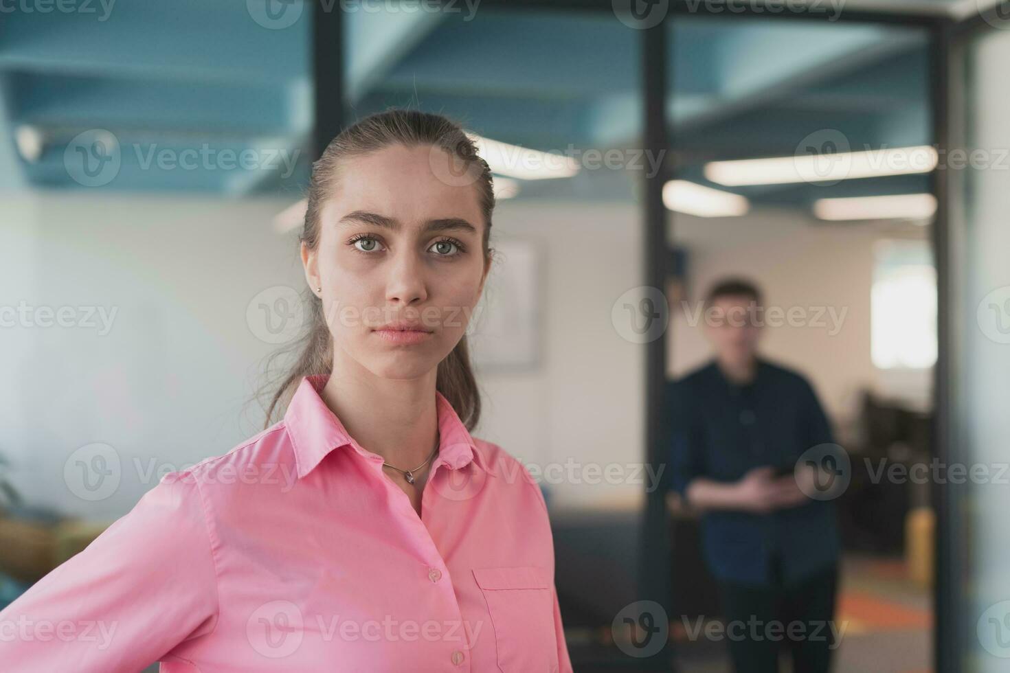 Portrait of young smiling business woman in creative open space coworking startup office. Successful businesswoman standing in office with copyspace. Coworkers working in background. photo