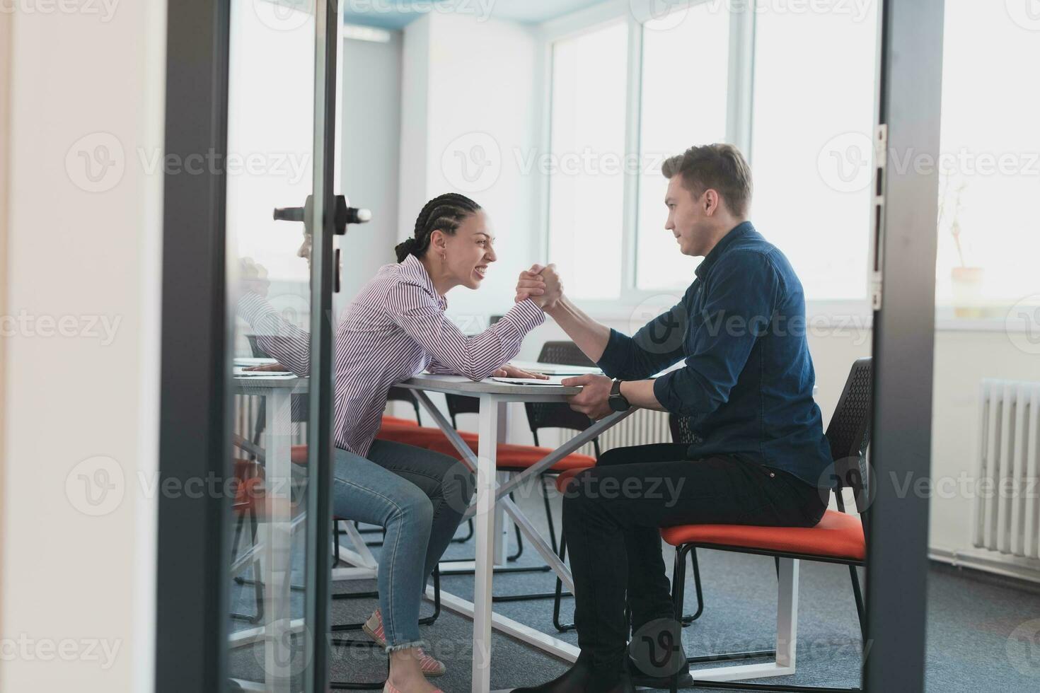 Businesspeople, rivalry and people concept - businesswoman and businessman arm wrestling during corporate meeting in modern bright open space coworking startup business office. photo