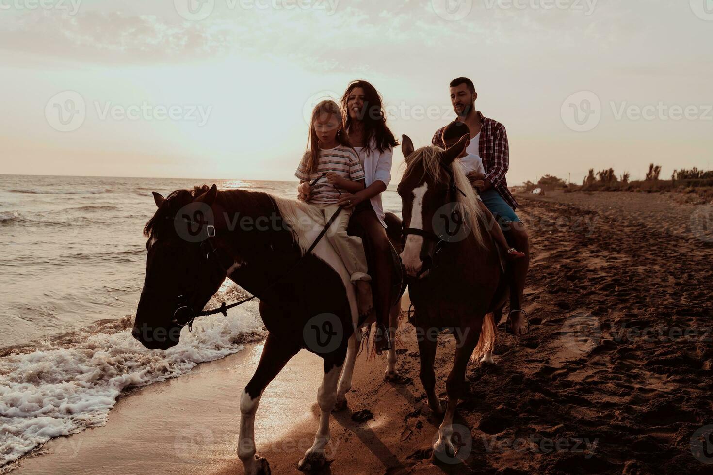 The family spends time with their children while riding horses together on a sandy beach. Selective focus photo