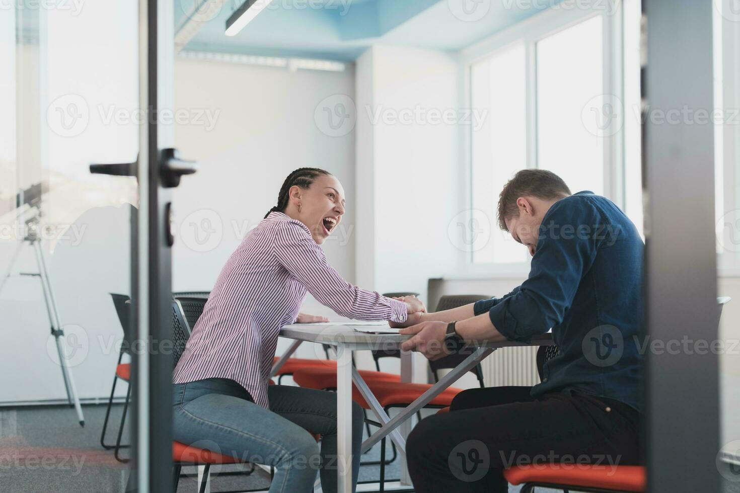 Businesspeople, rivalry and people concept - businesswoman and businessman arm wrestling during corporate meeting in modern bright open space coworking startup business office. photo