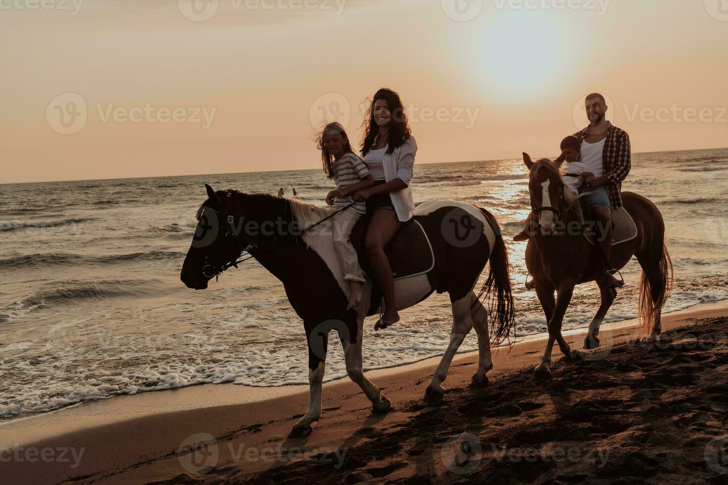 The family spends time with their children while riding horses together on a sandy beach. Selective focus photo