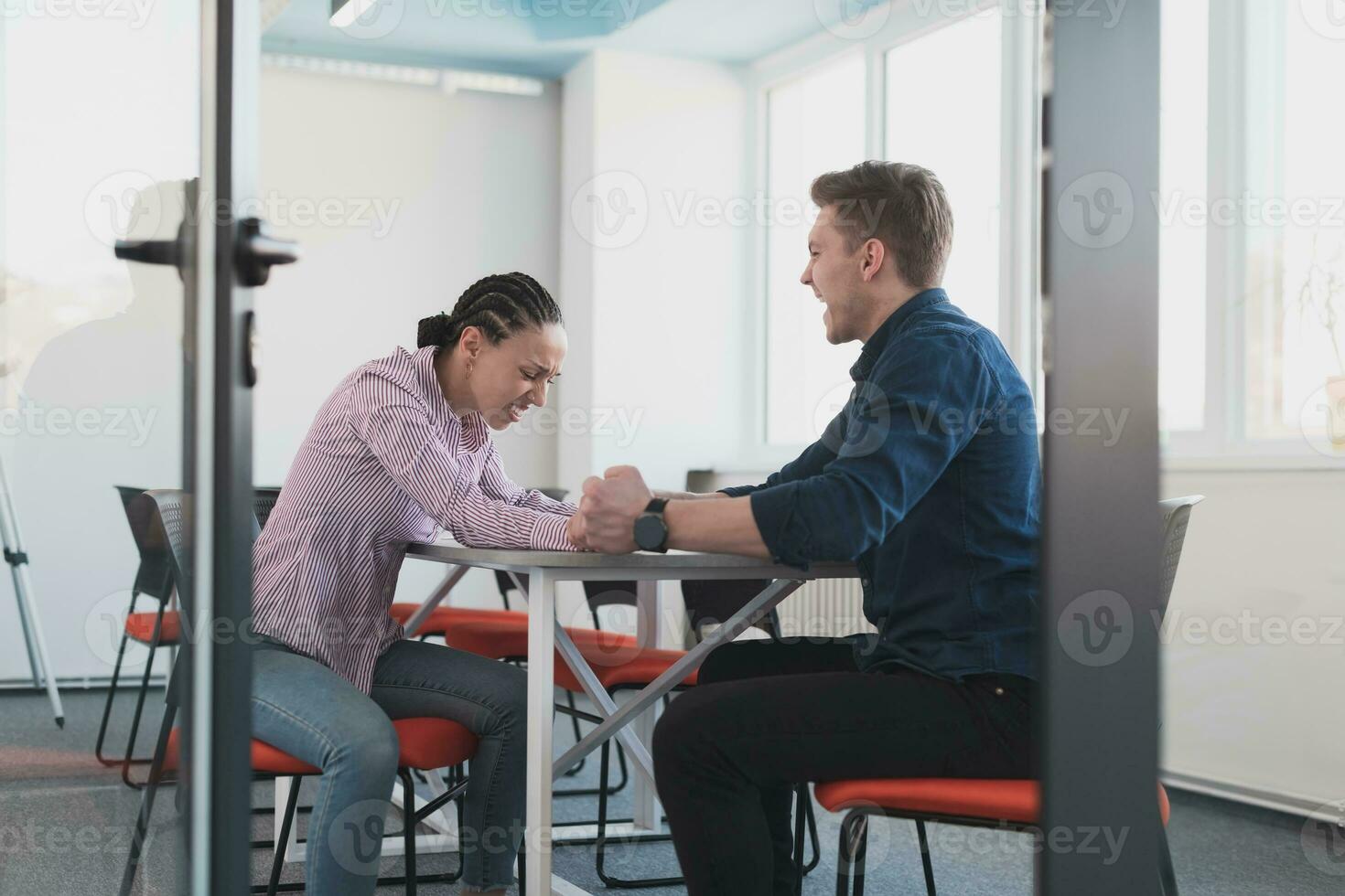 Businesspeople, rivalry and people concept - businesswoman and businessman arm wrestling during corporate meeting in modern bright open space coworking startup business office. photo