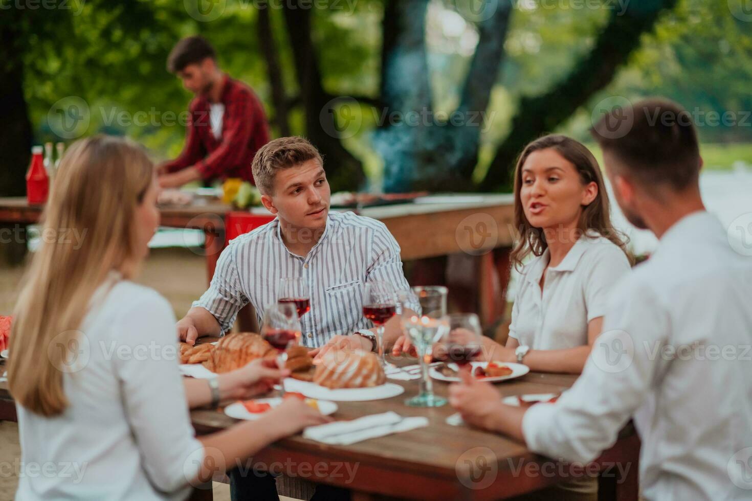 Group of happy friends having picnic french dinner party outdoor during summer holiday vacation near the river at beautiful nature photo