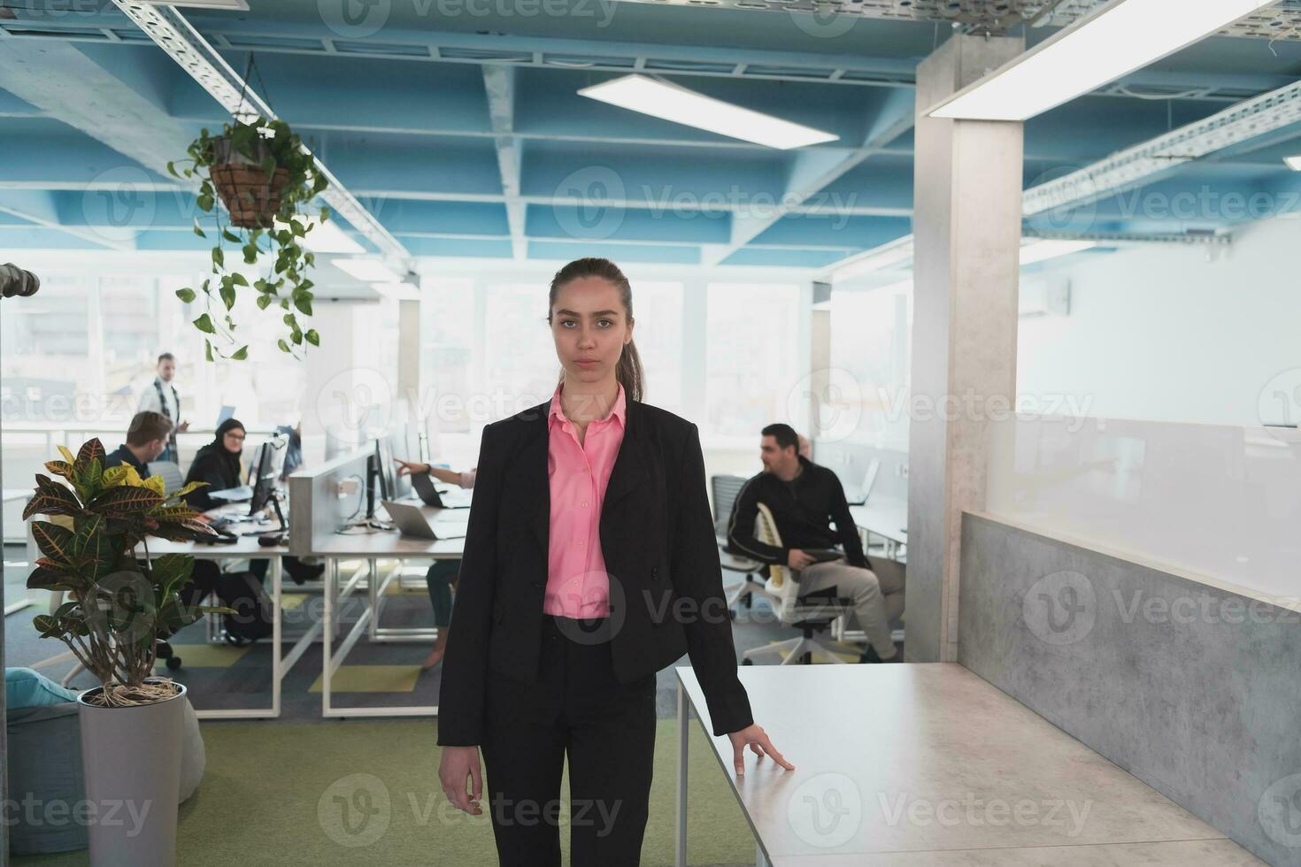 Portrait of young smiling business woman in creative open space coworking startup office. Successful businesswoman standing in office with copyspace. Coworkers working in background. photo