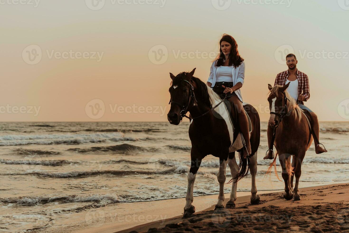 una pareja amorosa vestida de verano montando a caballo en una playa de arena al atardecer. mar y puesta de sol de fondo. enfoque selectivo foto