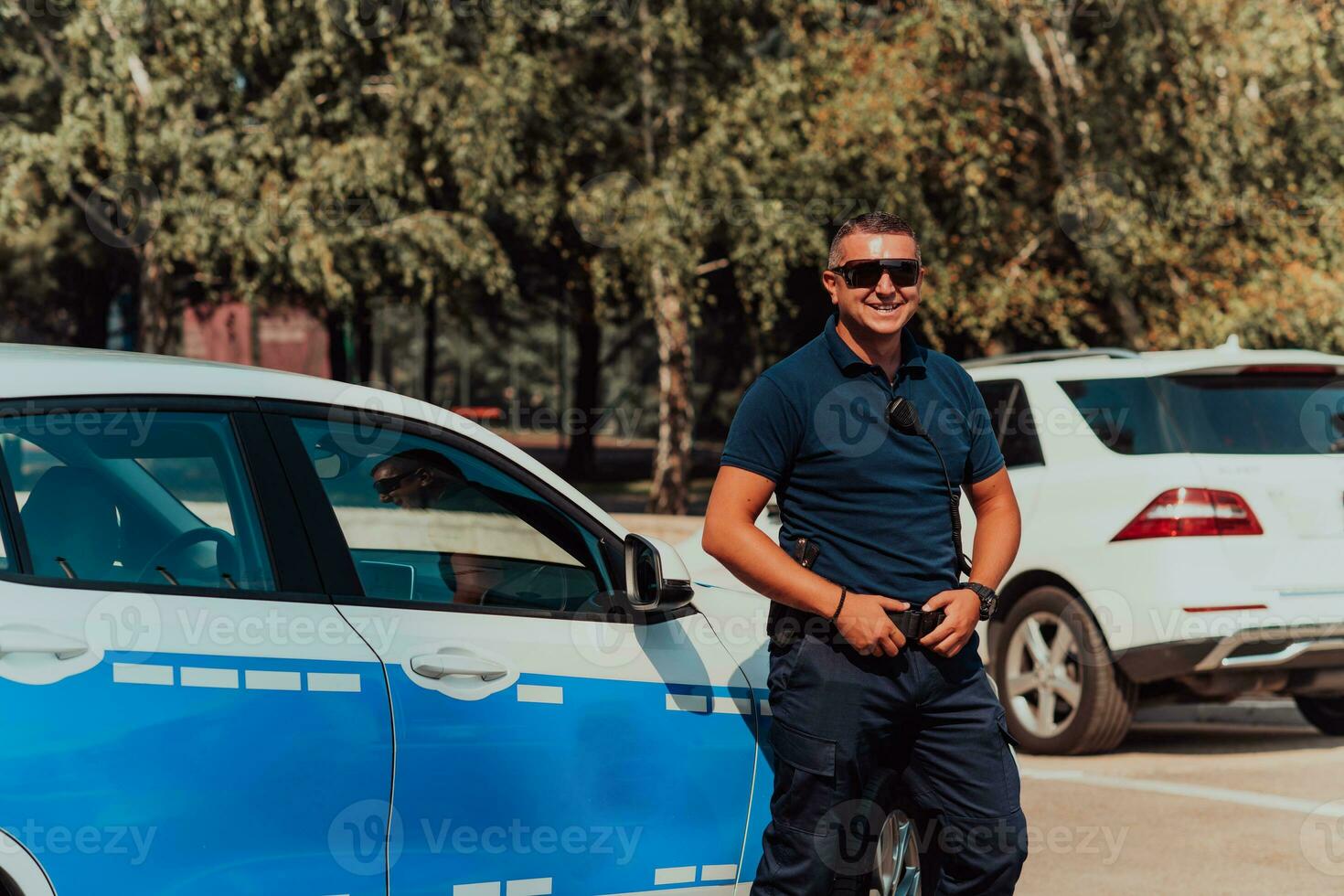 A policeofficer patrols the city. A police officer with sunglasses patroling in the city with an official police car photo