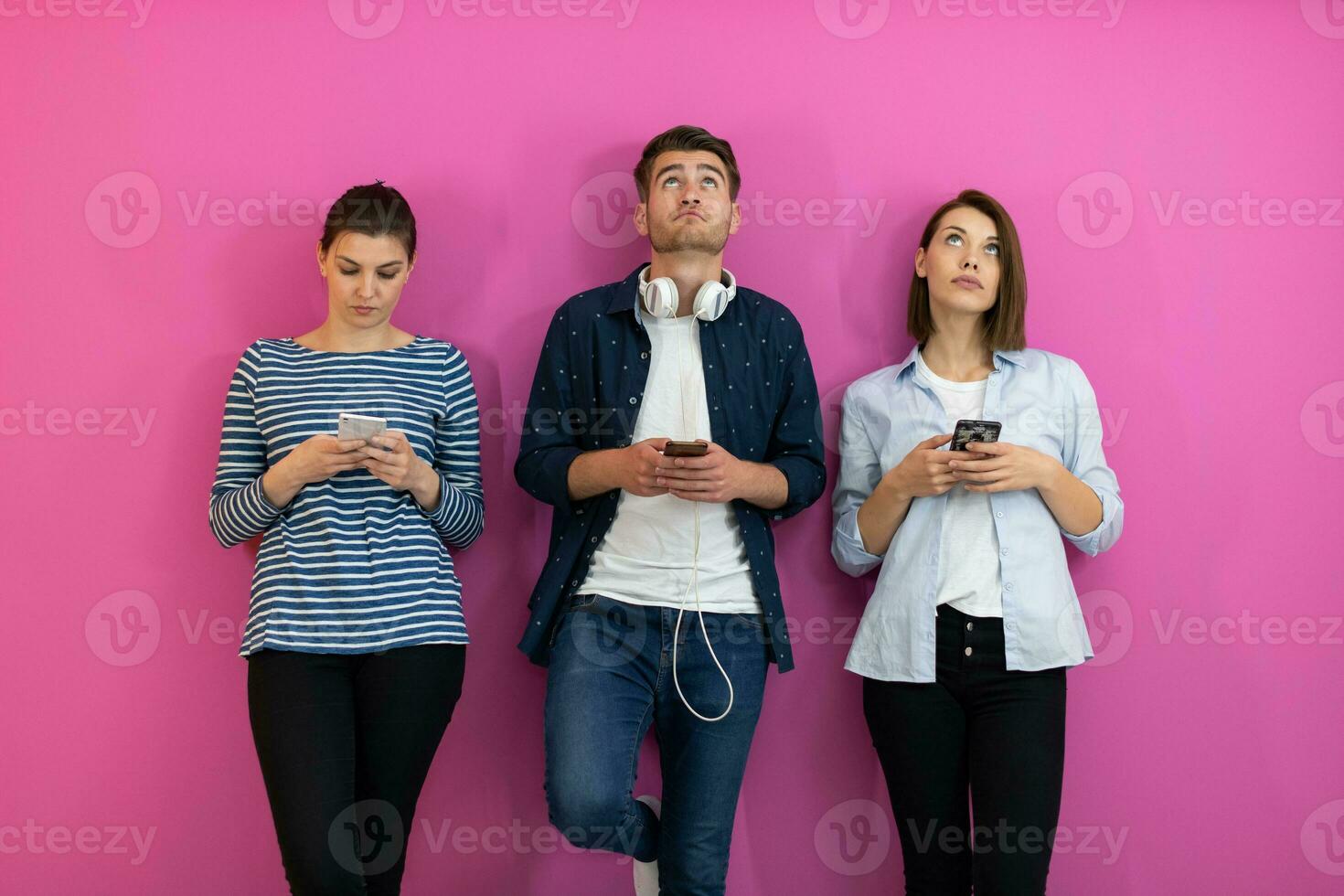 Diverse teenagers using smartphone while posing for a studio photo in front of a pink background