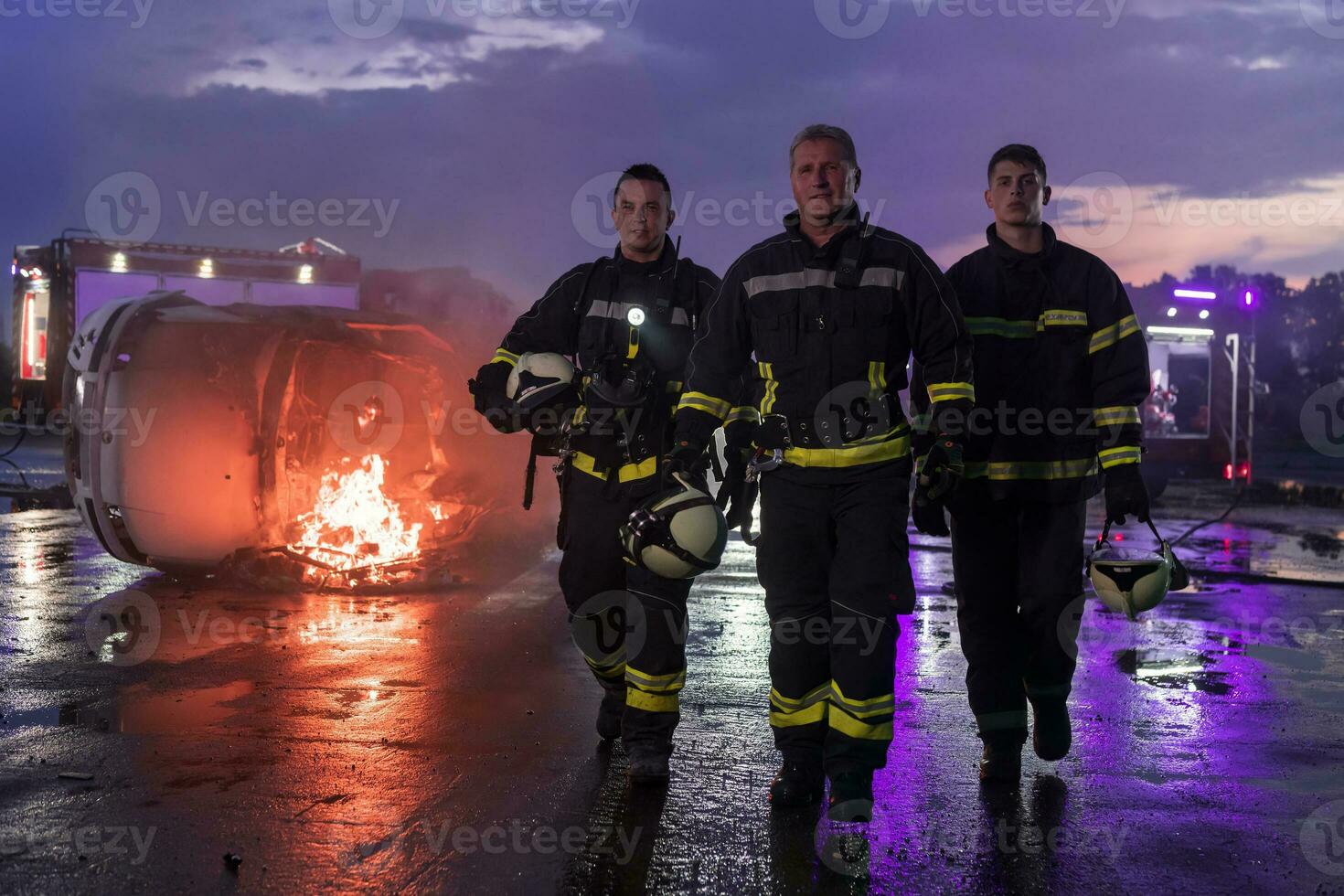Brave Firefighters Team Walking to the Camera. In Background Paramedics and Firemen Rescue Team Fight Fire in Car Accident, Insurance and Save Peoples Lives concept. photo