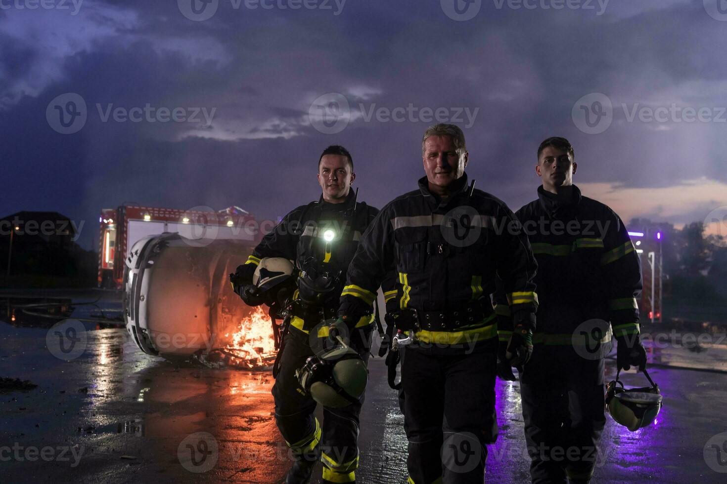 Brave Firefighters Team Walking to the Camera. In Background Paramedics and Firemen Rescue Team Fight Fire in Car Accident, Insurance and Save Peoples Lives concept. photo