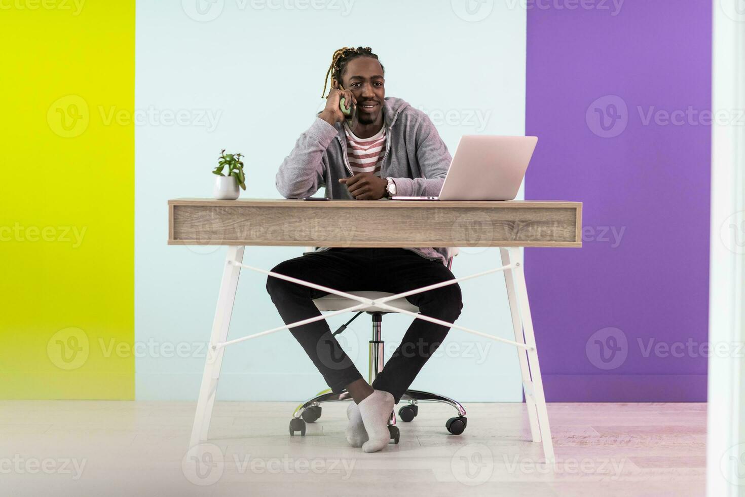 Smiling young african man freelancer using laptop and smartphone studying online working from home photo