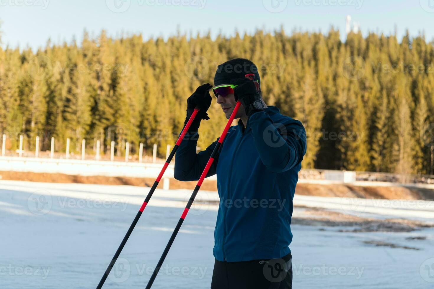 Handsome male athlete with cross country skis preparing equipment for training in a snowy forest. Checking smartwatch. Healthy winter lifestyle. photo