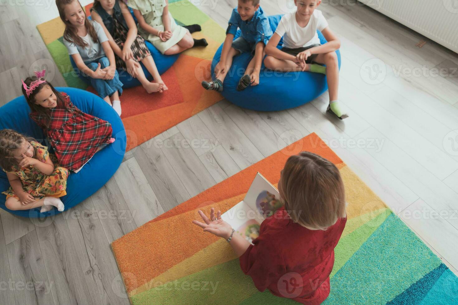 Reading time in an elementary school or kindergarten, a teacher reads a book to children in an elementary school or kindergarten. The concept of pre-school education. Selective focus photo