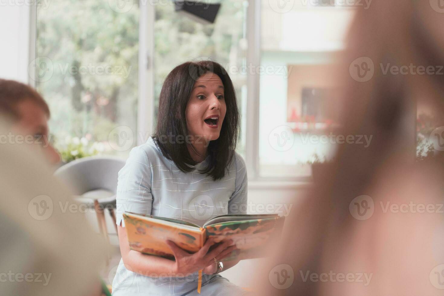 Reading time in an elementary school or kindergarten, a teacher reads a book to children in an elementary school or kindergarten. The concept of pre-school education. Selective focus photo