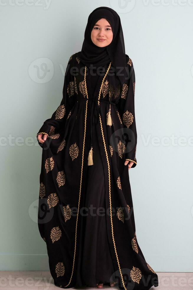 beautiful muslim woman in fashinable dress with hijab isolated on modern cyan background representing concept of modern islam and ramadan kareem photo