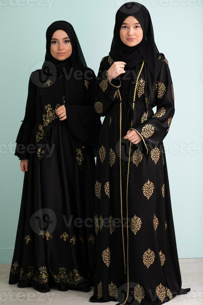 Two beautiful muslim woman in fashinable dress with hijab isolated on modern cyan background representing concept of modern islam and ramadan kareem photo