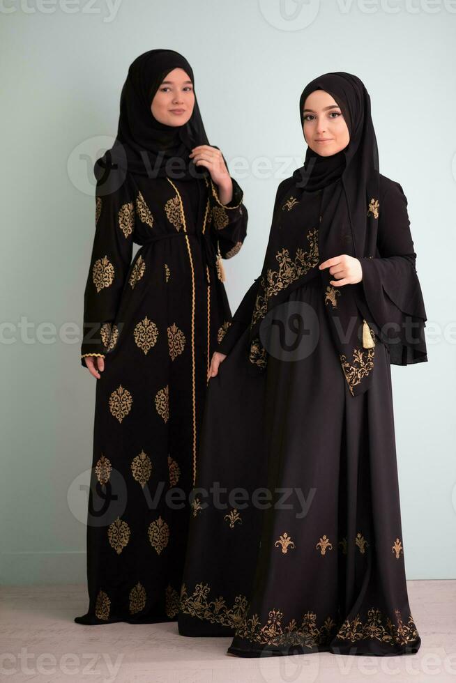 Two beautiful muslim woman in fashinable dress with hijab isolated on modern cyan background representing concept of modern islam and ramadan kareem photo