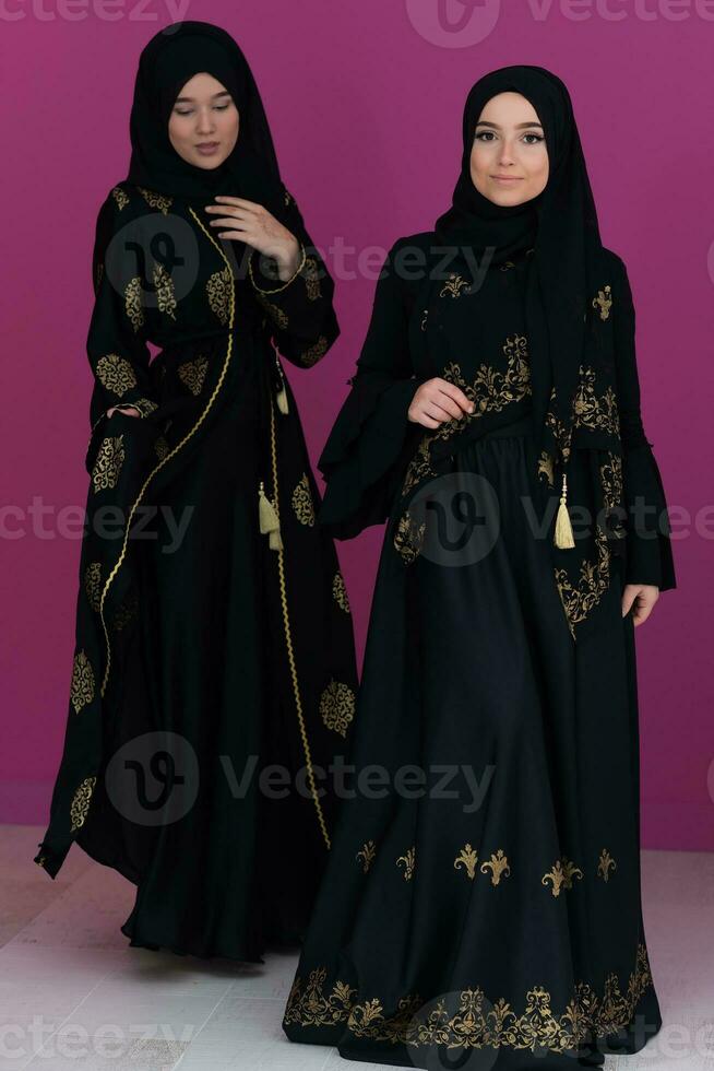 Two beautiful muslim woman in fashinable dress with hijab isolated on modern pink background representing concept of modern islam and ramadan kareem photo