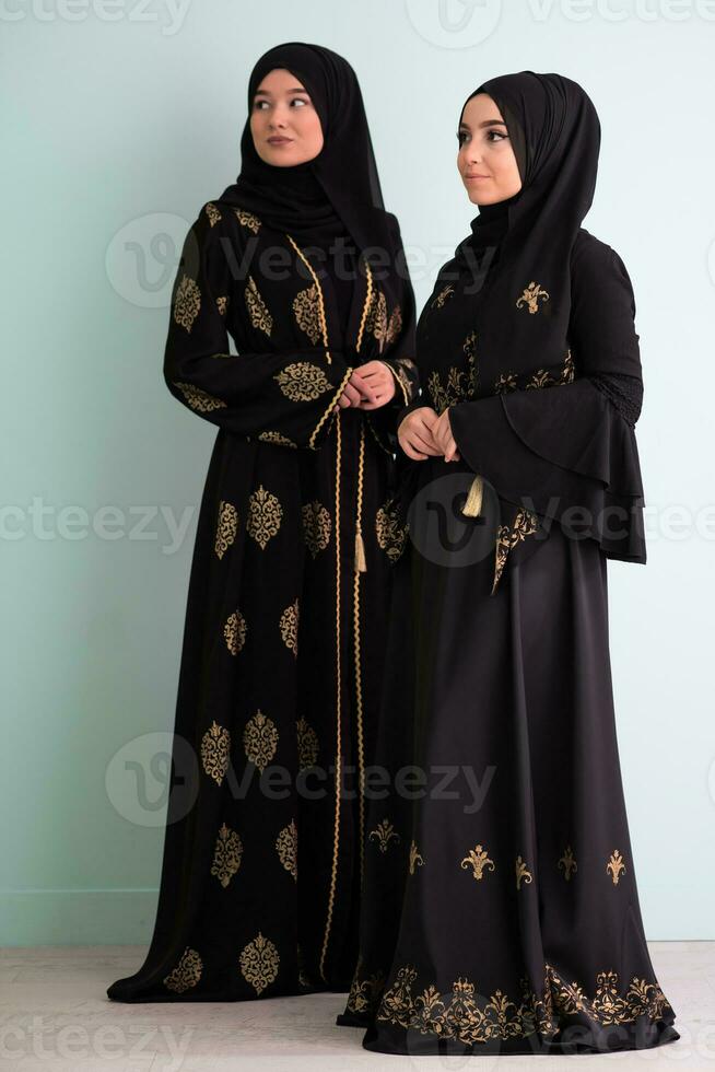 Two beautiful muslim woman in fashinable dress with hijab isolated on modern cyan background representing concept of modern islam and ramadan kareem photo