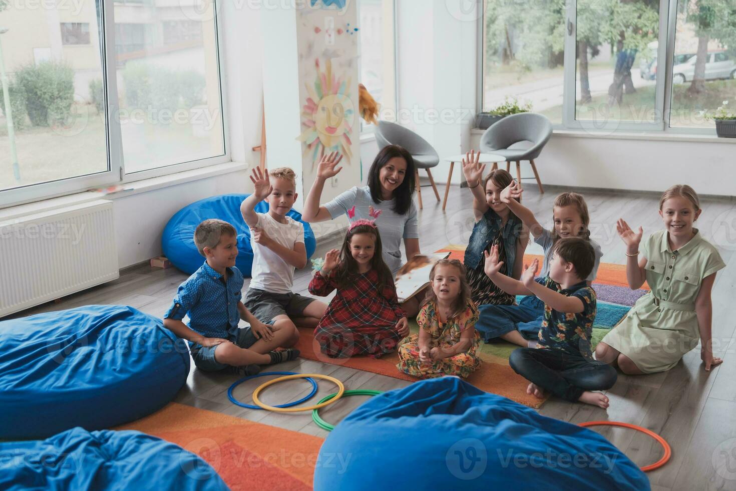 un contento hembra profesor sentado y jugando mano juegos con un grupo de pequeño Niños de escuela foto