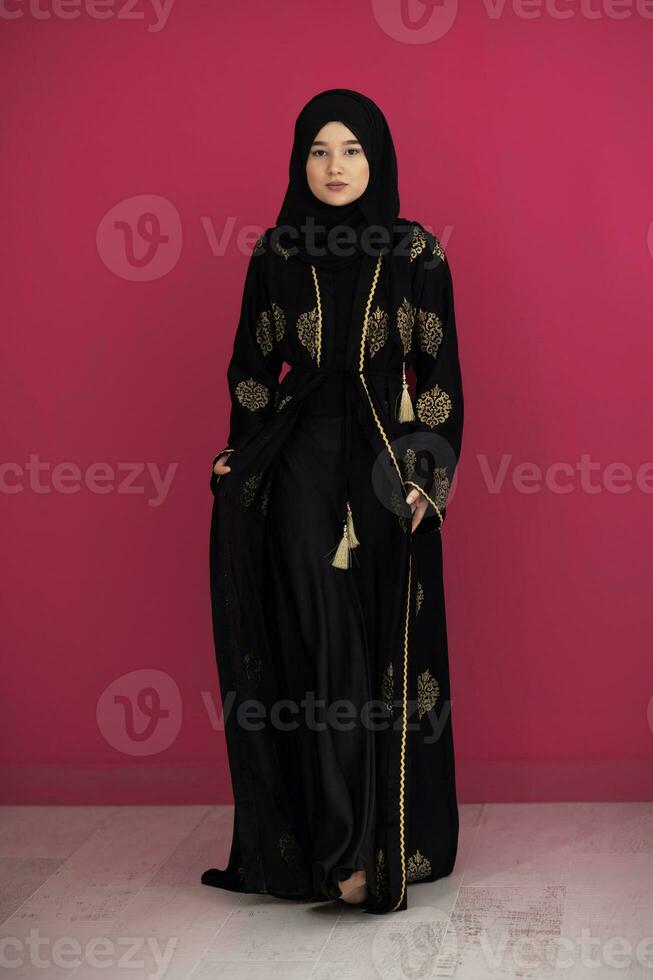 beautiful muslim woman in fashinable dress with hijab isolated on modern red background representing concept of modern islam and ramadan kareem photo