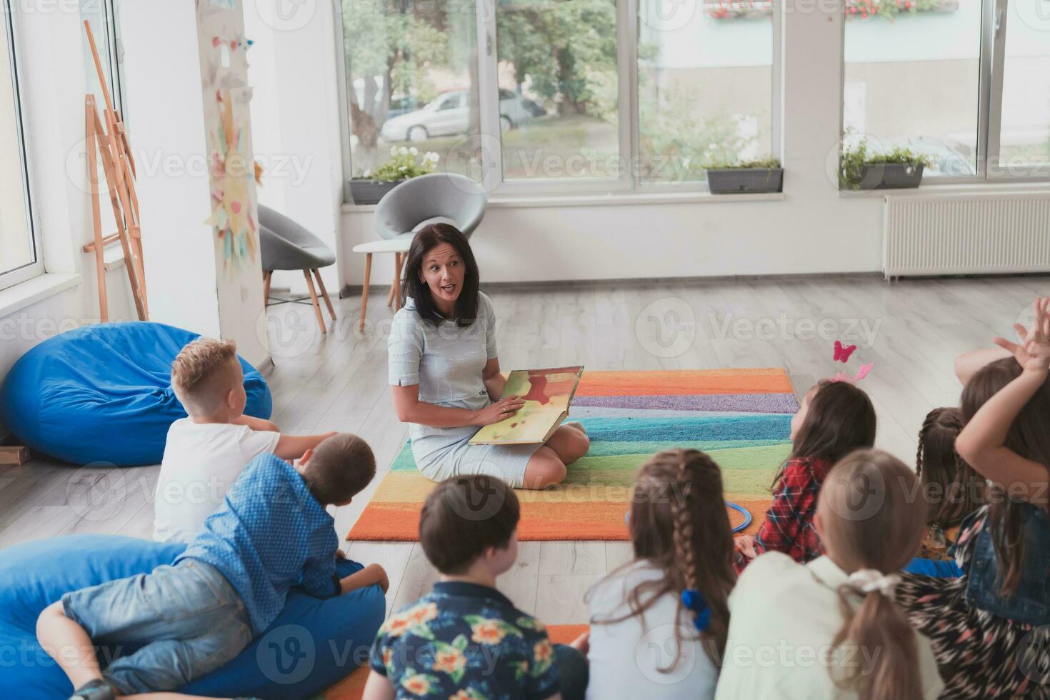 A happy female teacher sitting and playing hand games with a group of little schoolchildren photo