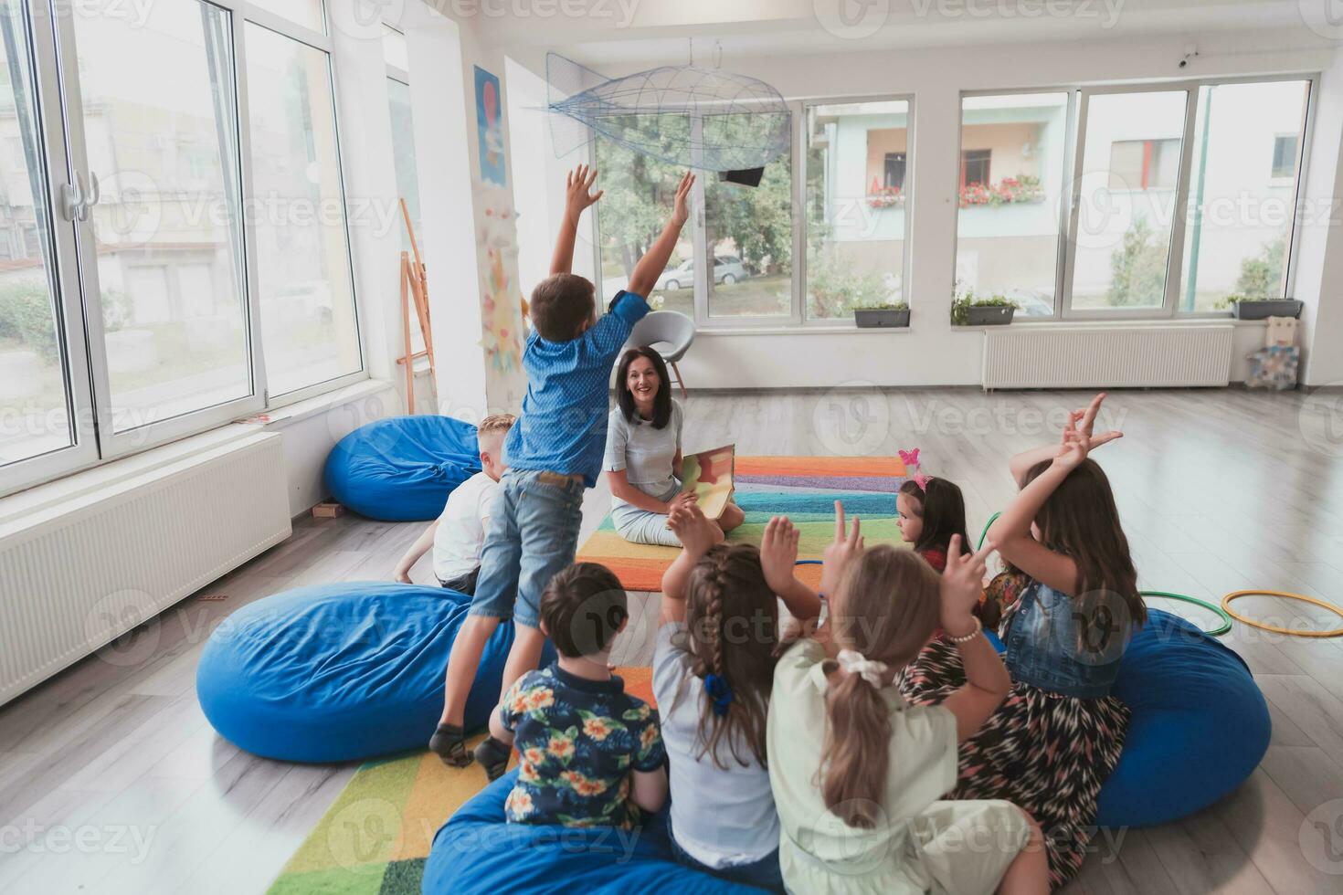 A happy female teacher sitting and playing hand games with a group of little schoolchildren photo