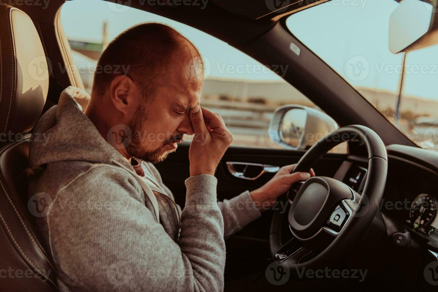 A tired driver holding his head. Exhausted and tired driver driving a car at sunset photo