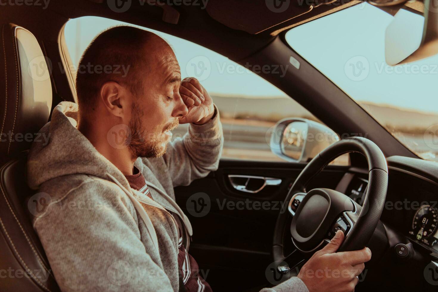 A tired driver holding his head. Exhausted and tired driver driving a car at sunset photo