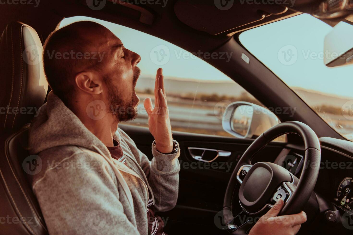 A tired driver yawns while driving a car at sunset photo