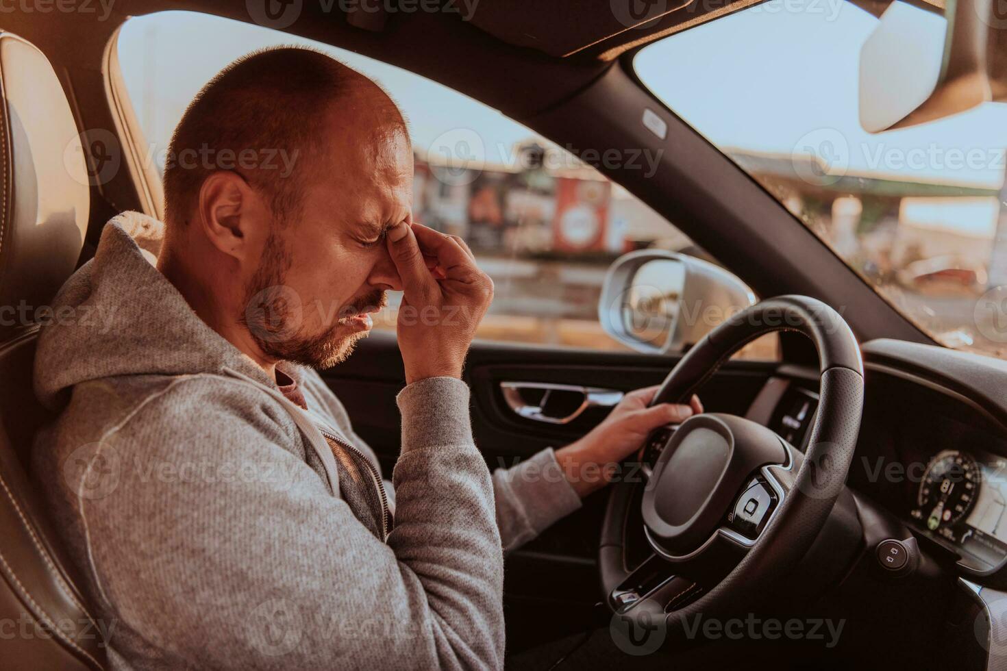 A tired driver holding his head. Exhausted and tired driver driving a car at sunset photo