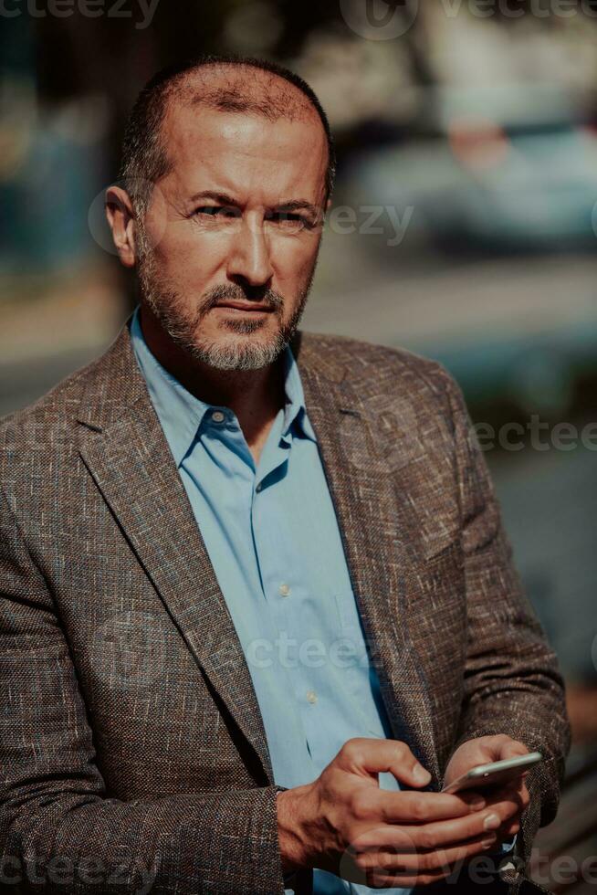 Modern senior businessman in suit uses smartphone in urban environment. photo